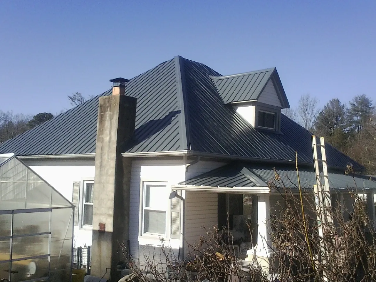 Dark blue standing seam metal roof on a white farmhouse with dormer — Slate & Tile Roof Repair by Roofing Brothers in Baltimore