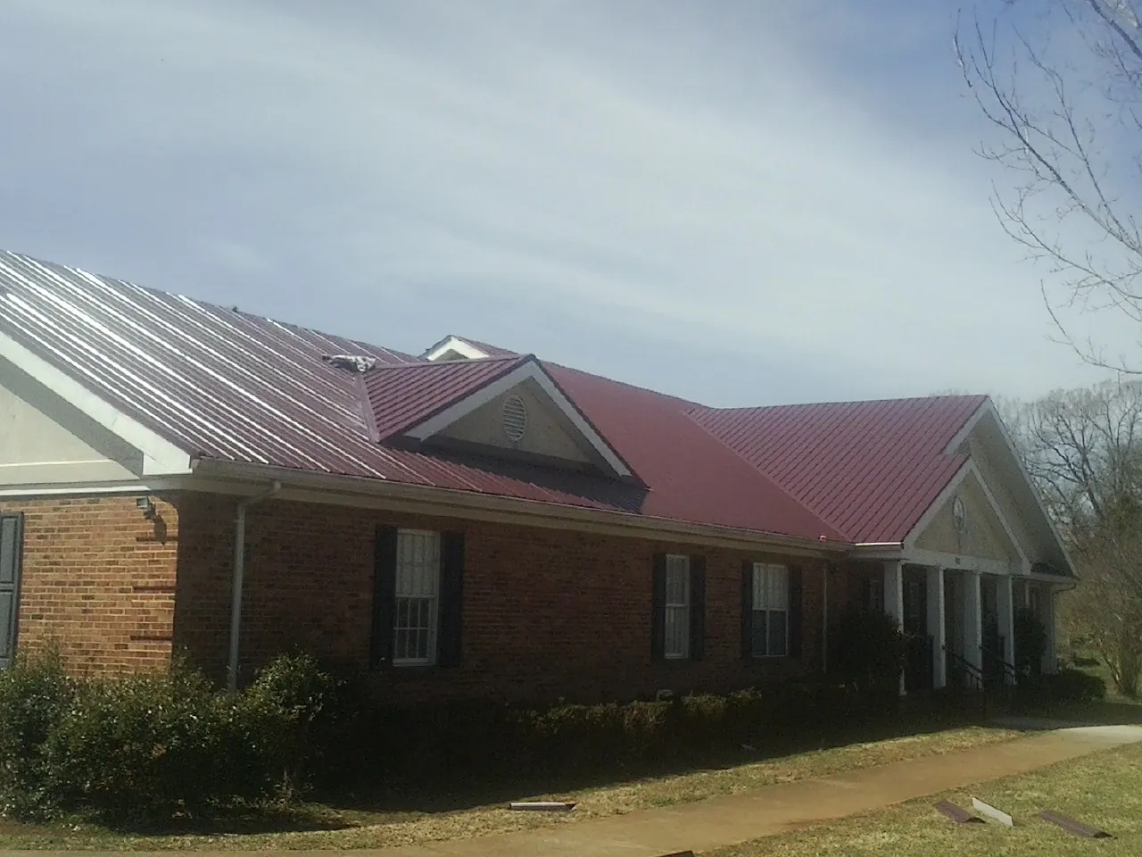 Red metal roof with gabled entries on a long brick building, from a Hail Damage Roof Repair job in Baltimore