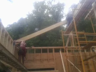 Carpenter raising a rafter beam on a new second story frame in Baltimore