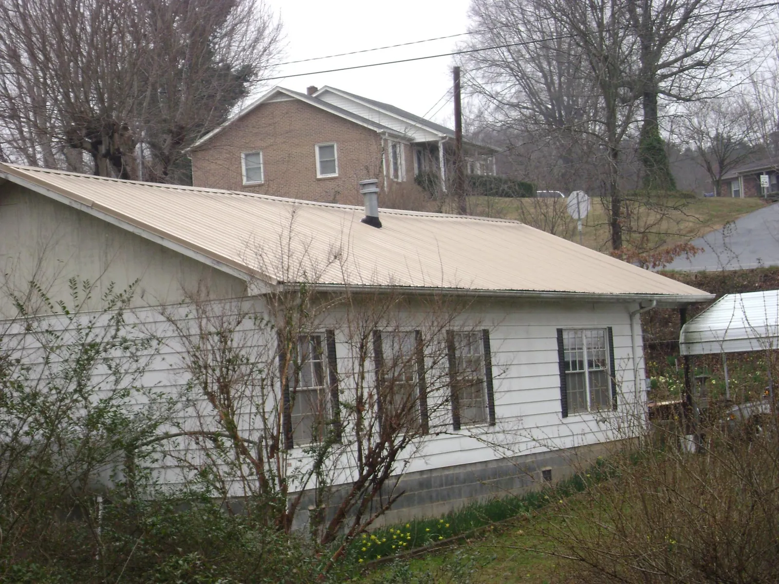 Tan metal roof on a white sided house set into a hillside — Commercial Roofing by Roofing Brothers in Baltimore